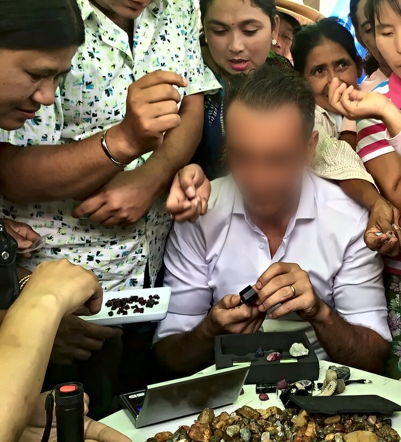 David Nataf au marché aux pierres de Mogok, 2016, examinant des pierres brutes entouré de vendeurs